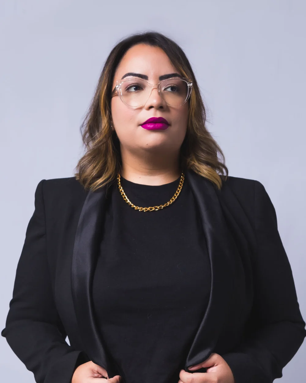 Amanda Noronha in a black blazer and gold necklace, studio portrait